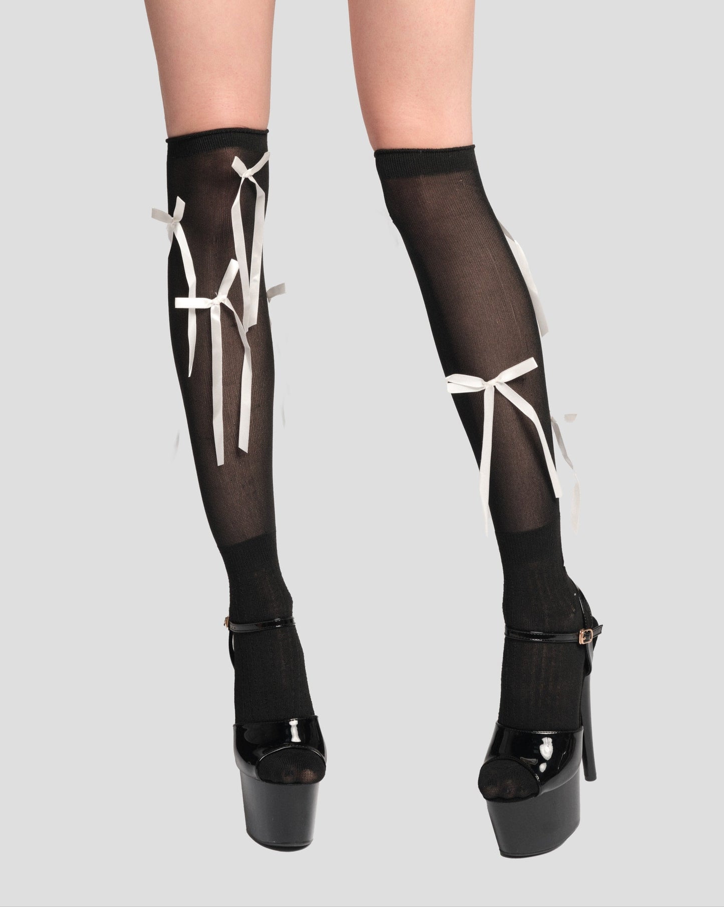 Black sheer stockings with white bows worn by a model on a gray background