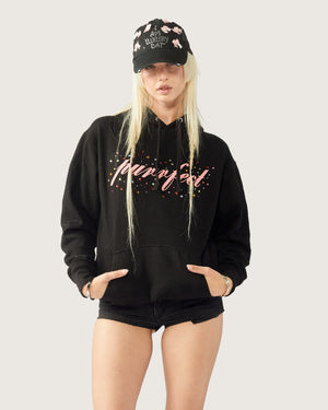 Person wearing a black hoodie and shorts with text, paired with a black cap on a light gray background