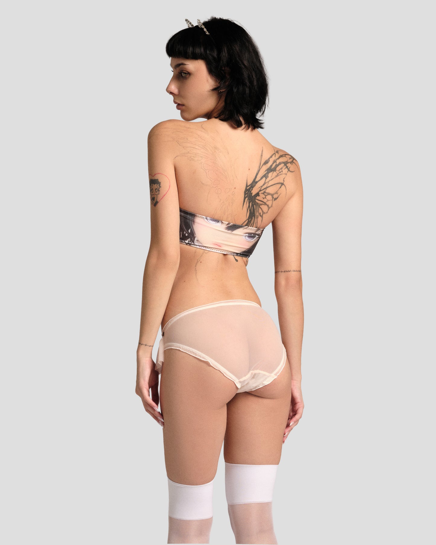 Person wearing a patterned bra and sheer pants on a plain background