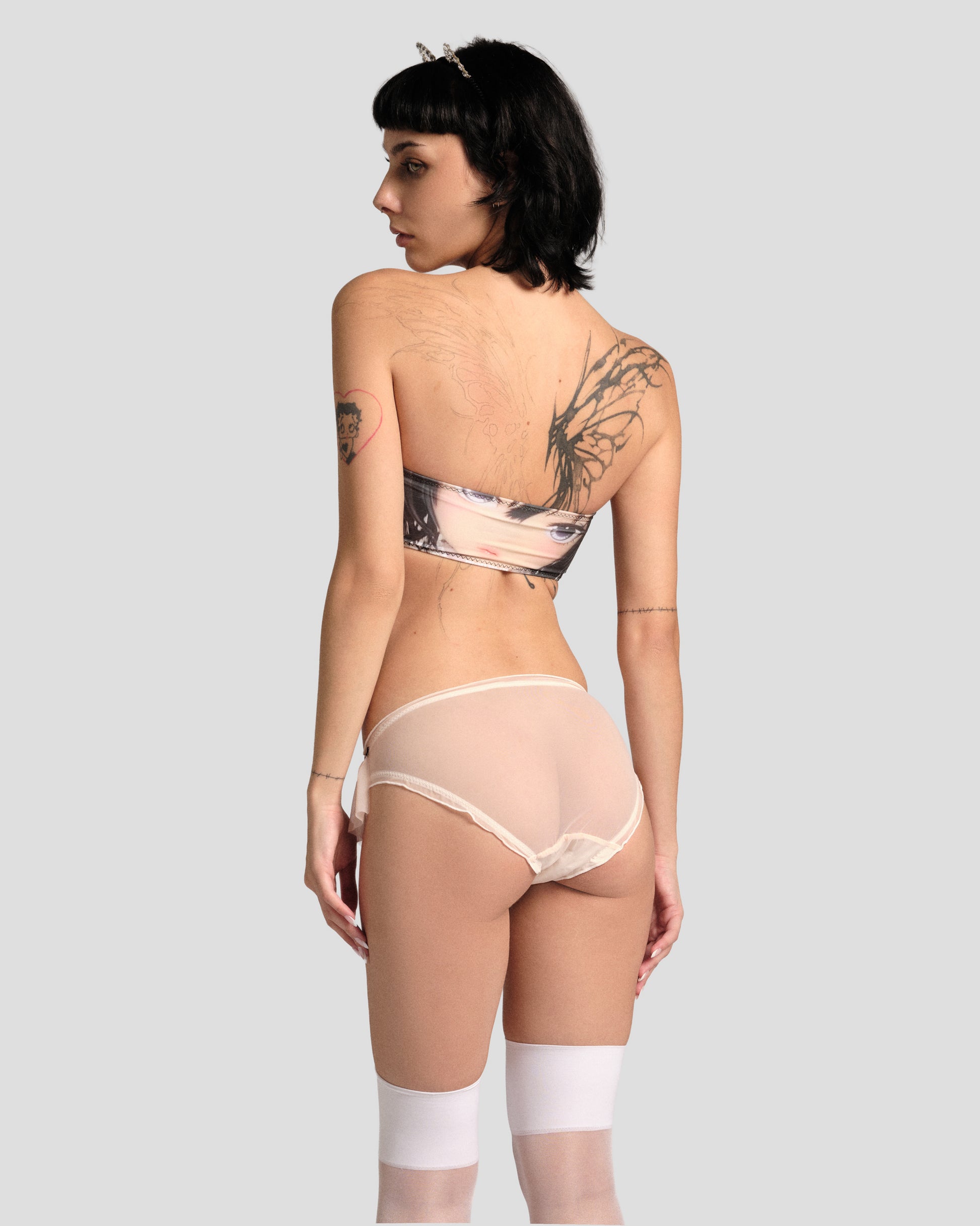 Person wearing a patterned bra and sheer pants on a plain background